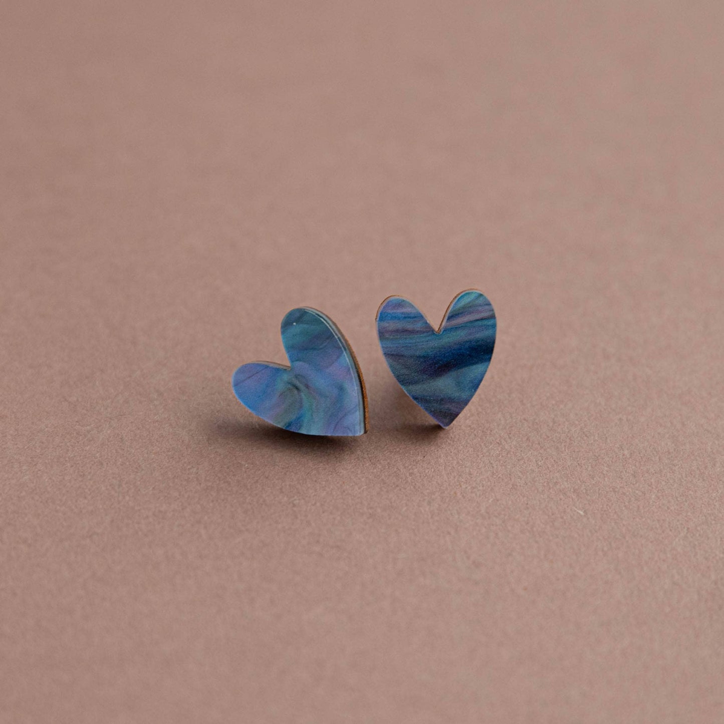 Heart-shaped earrings with blue marbled design on a brown background