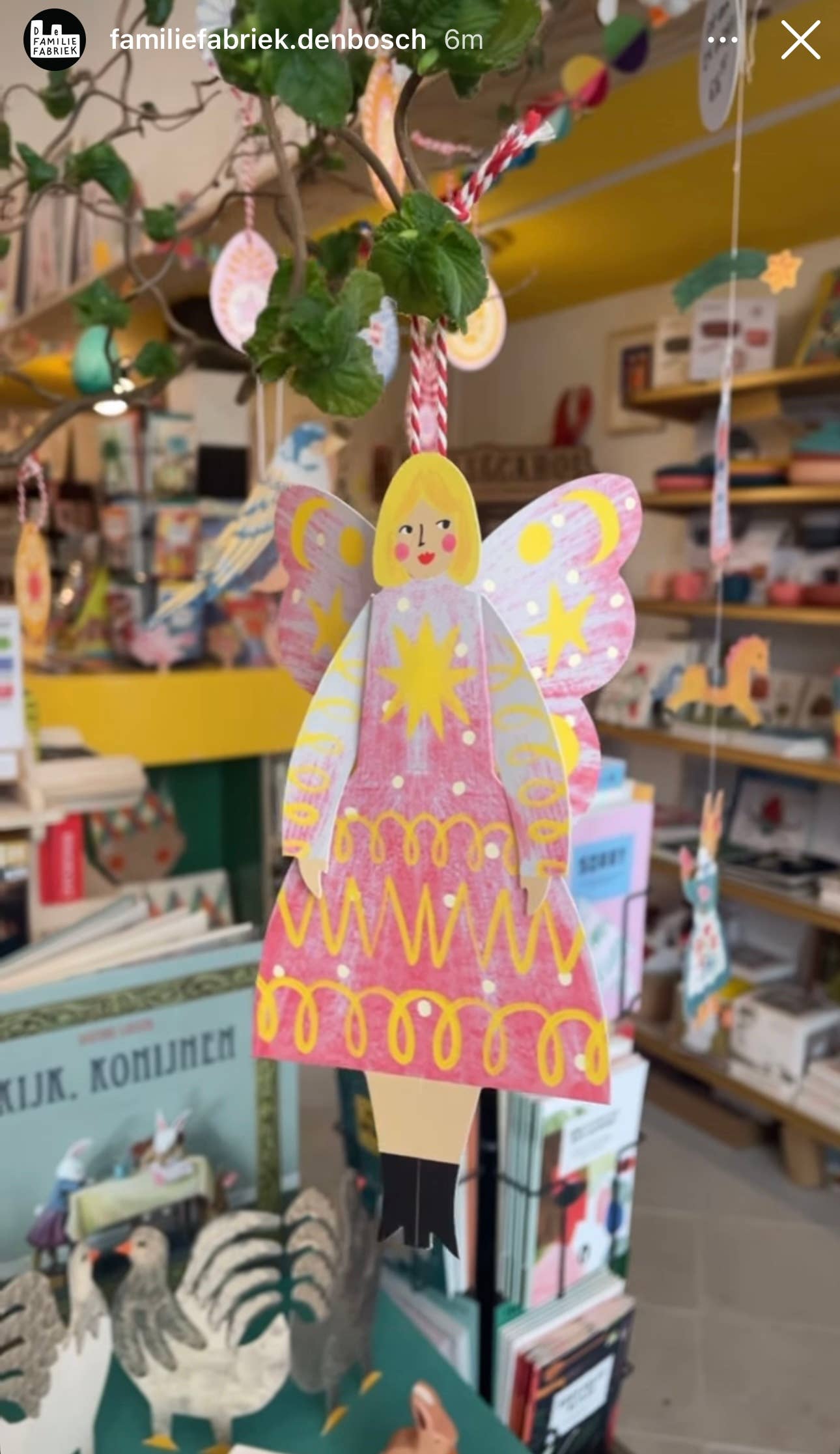 Decorative angel figure with pink dress and yellow hair hanging in a store.