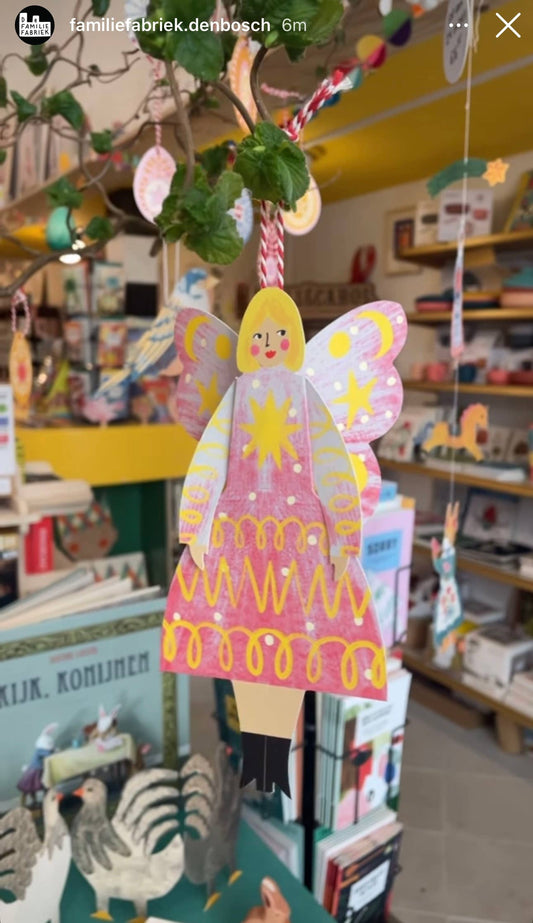 Decorative angel figure with pink dress and yellow hair hanging in a store.