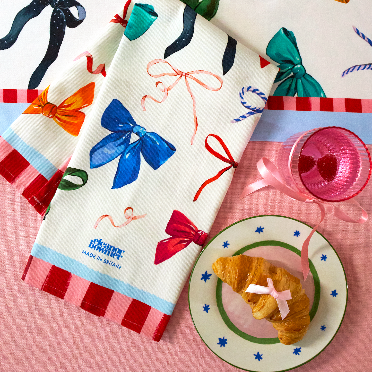 Decorative towels with colorful bows and ribbons on a pink surface with a croissant and plate.