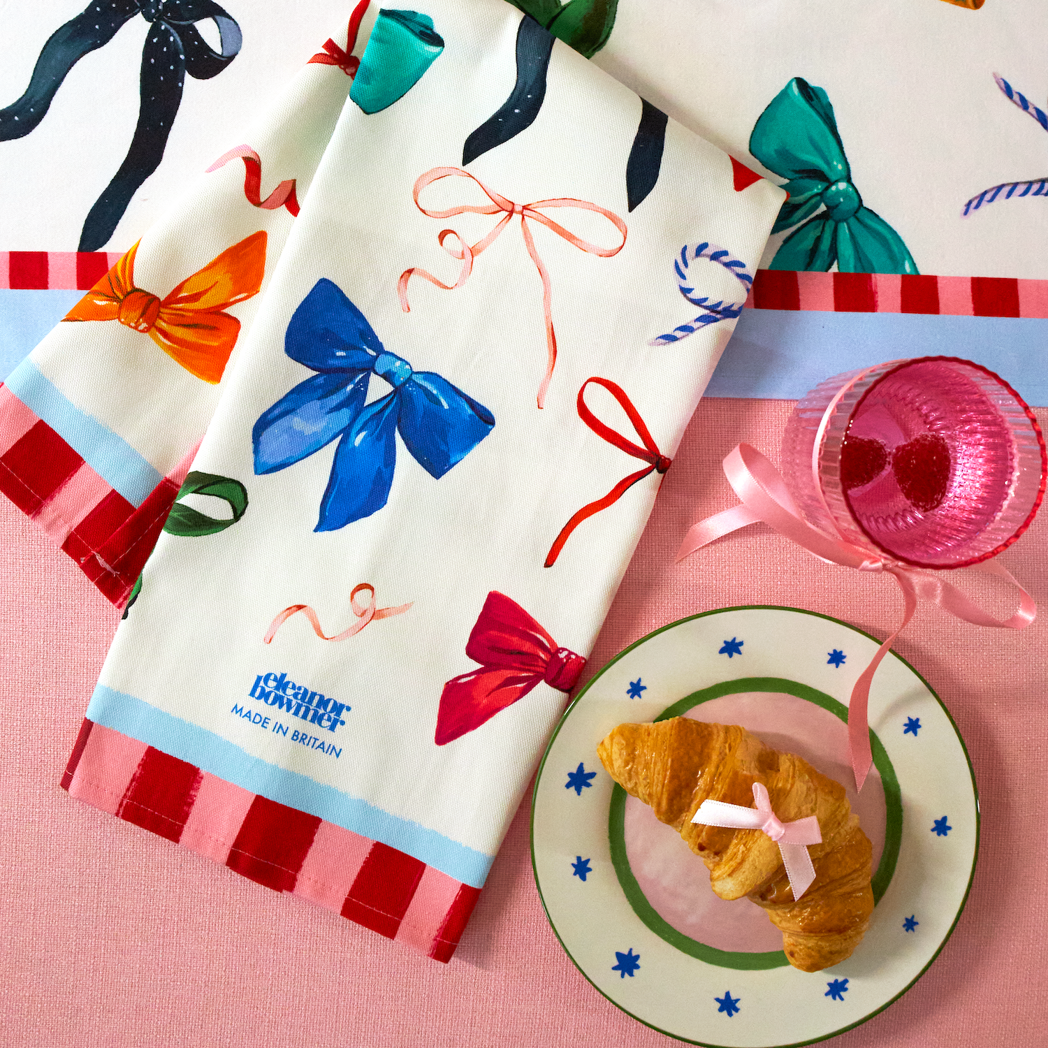 Decorative towels with colorful bows and ribbons on a pink surface with a croissant and plate.