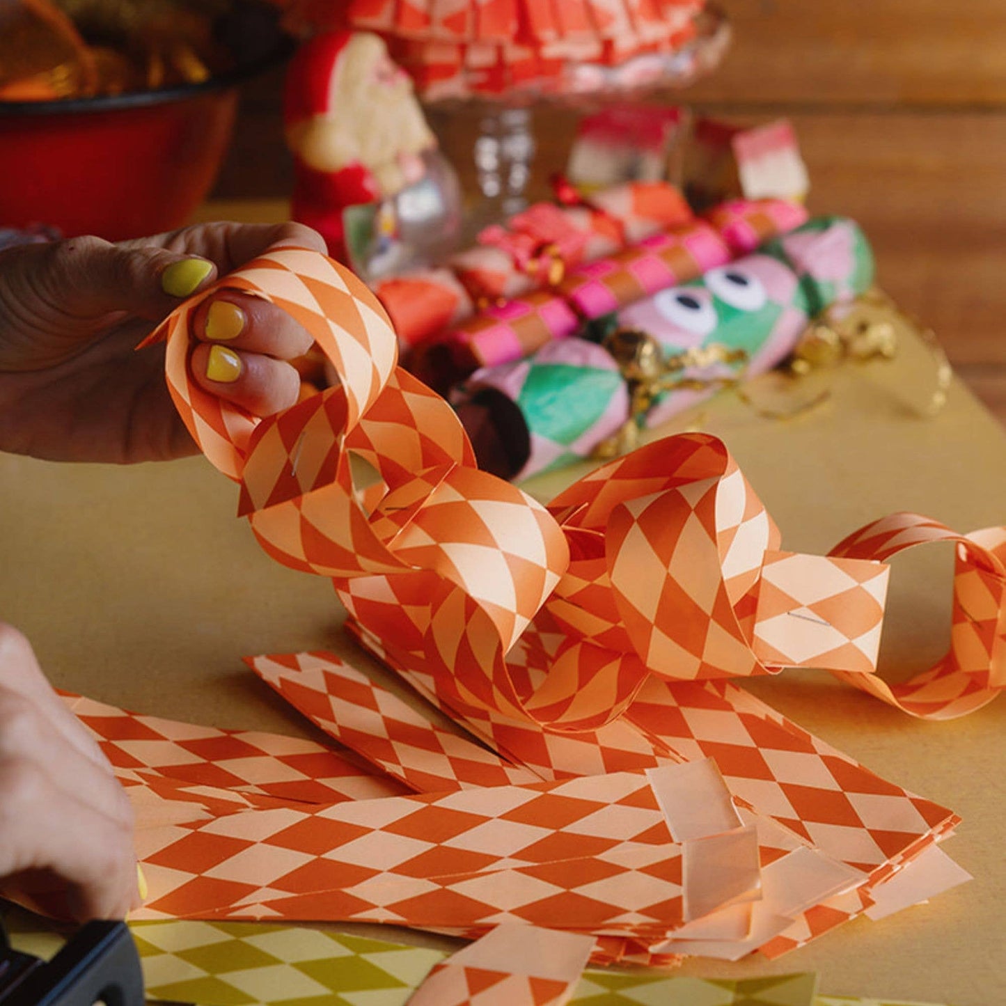 Person making a paper chain with orange and white checkered paper on a colorful background