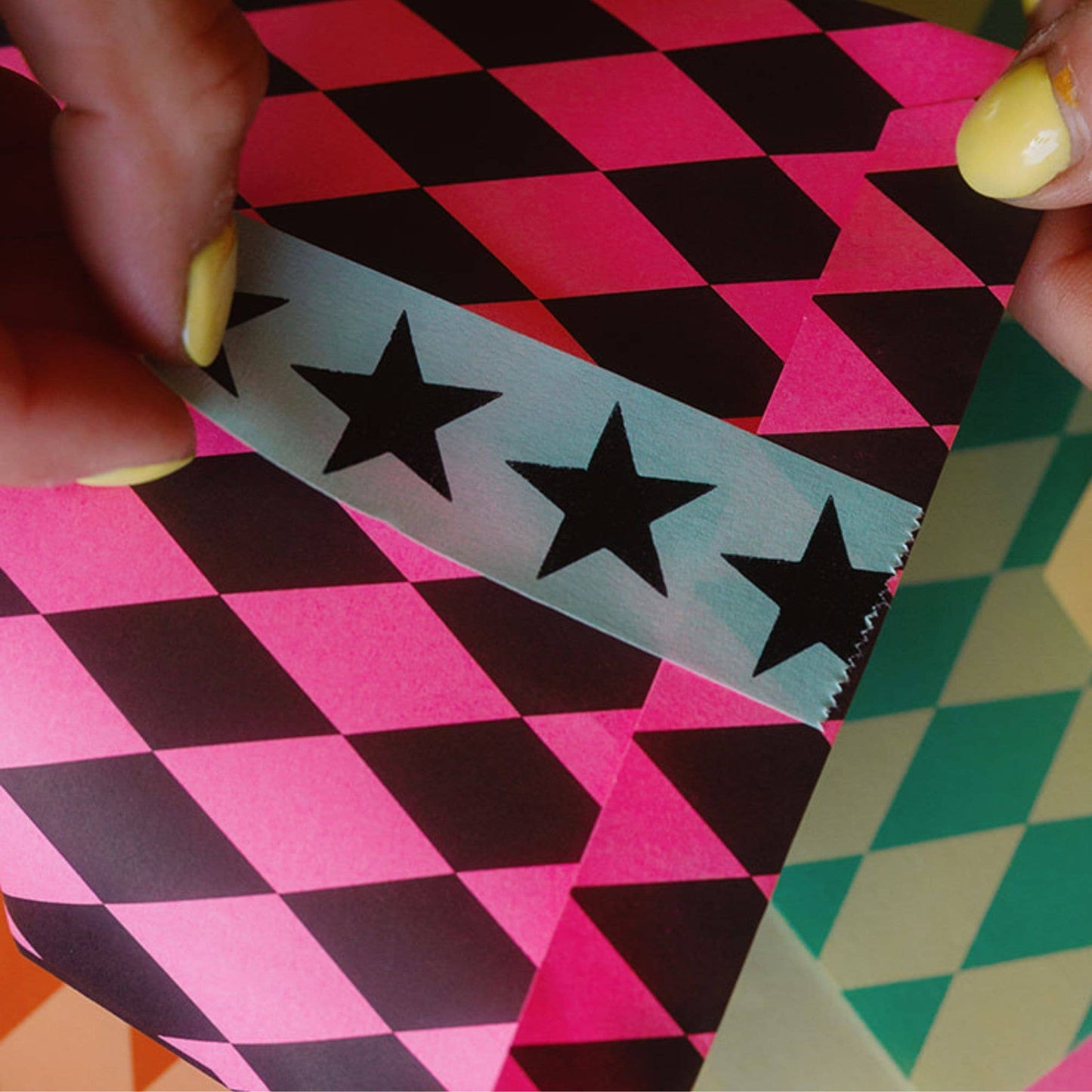 Person holding a pink, black, and teal geometric-patterned paper with star stickers.