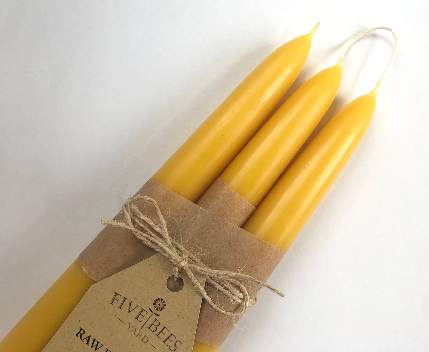 Three yellow candles tied with brown paper and string on a white background, featuring a 'Five Bees' label.