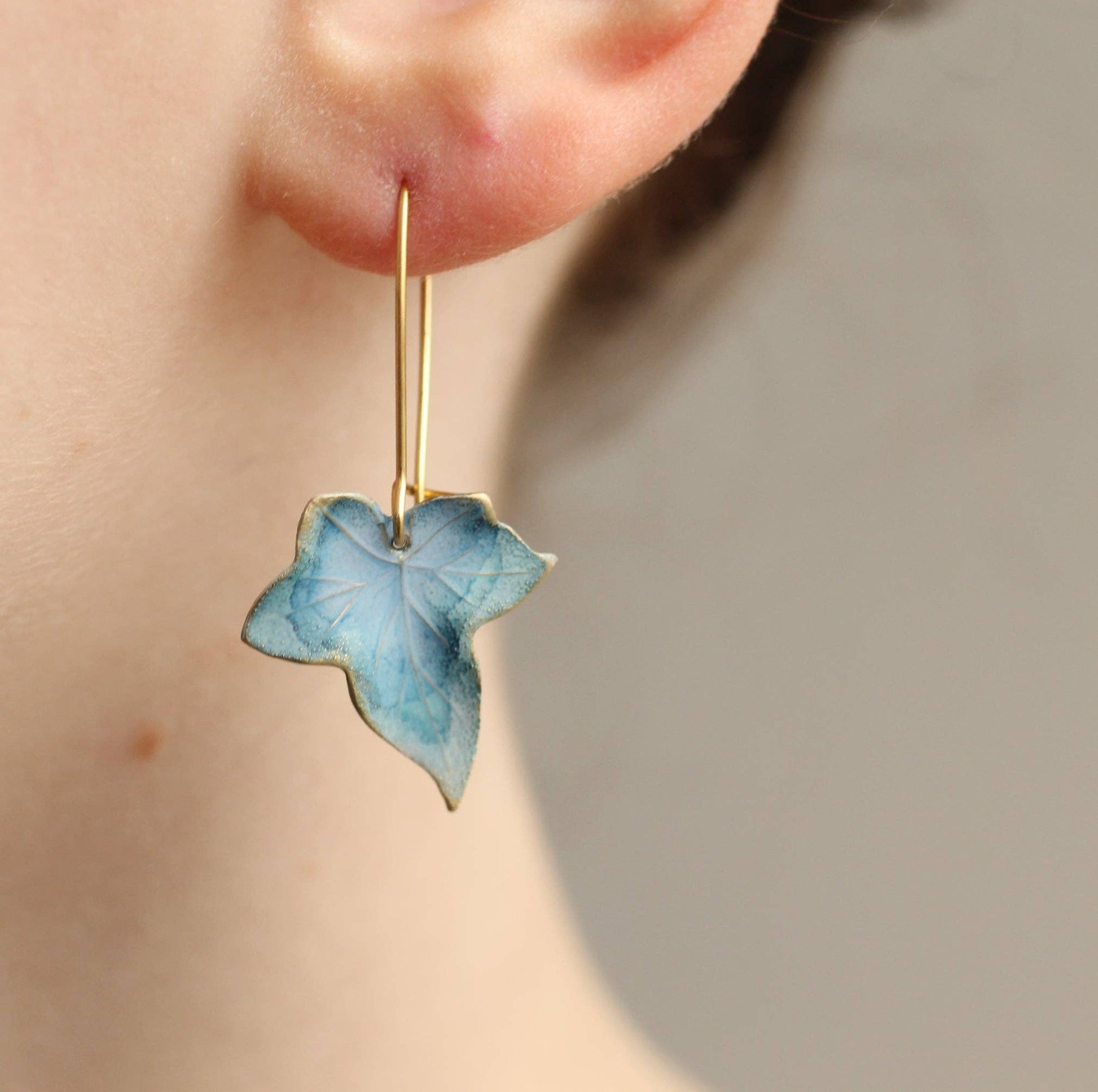 Blue leaf-shaped earring worn on a person's ear against a neutral background