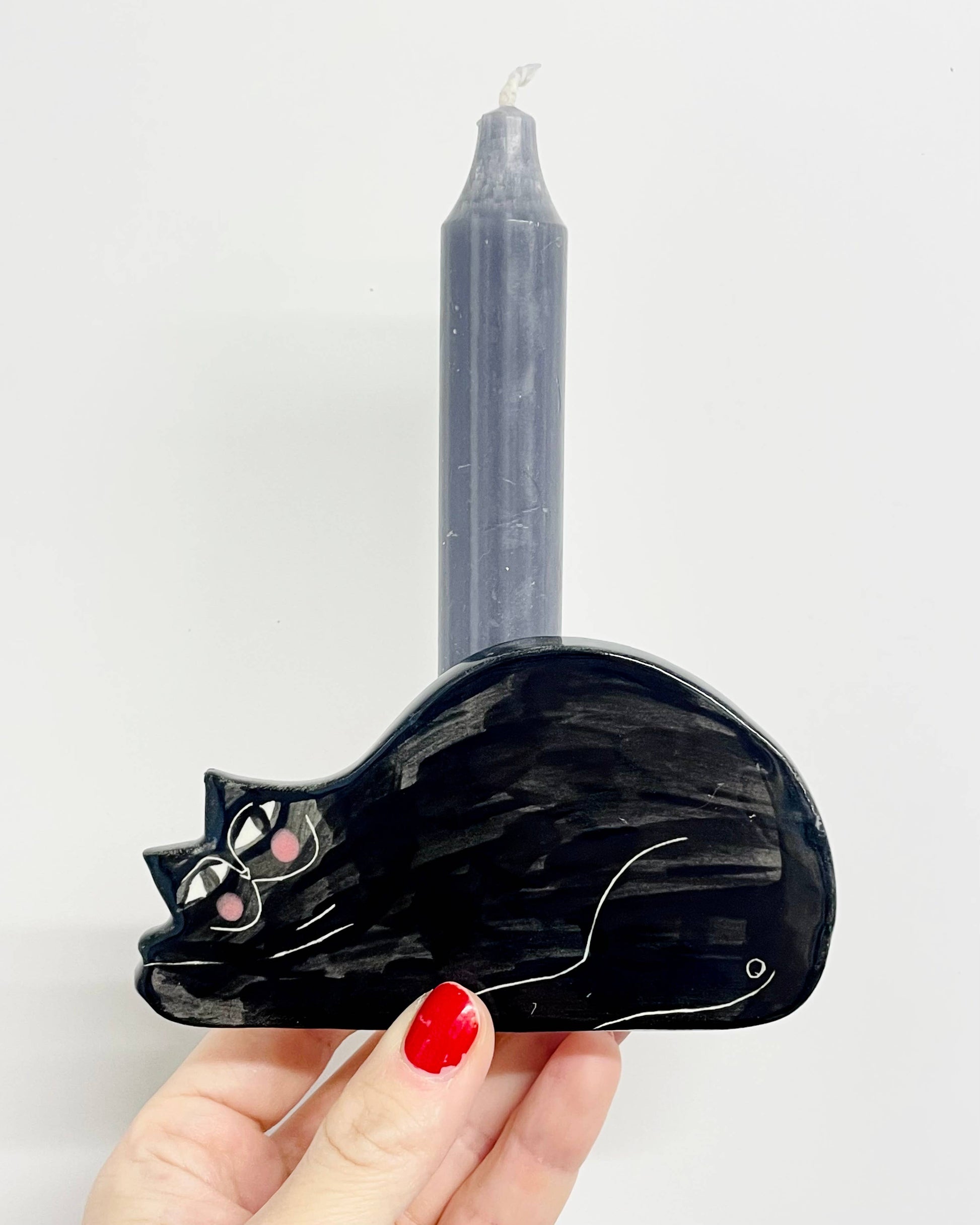 Black cat-shaped candle holder with a gray candle on a white background