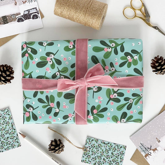 Gift wrapped in blue paper with green leaf pattern and pink ribbon on a white surface with decorative items.