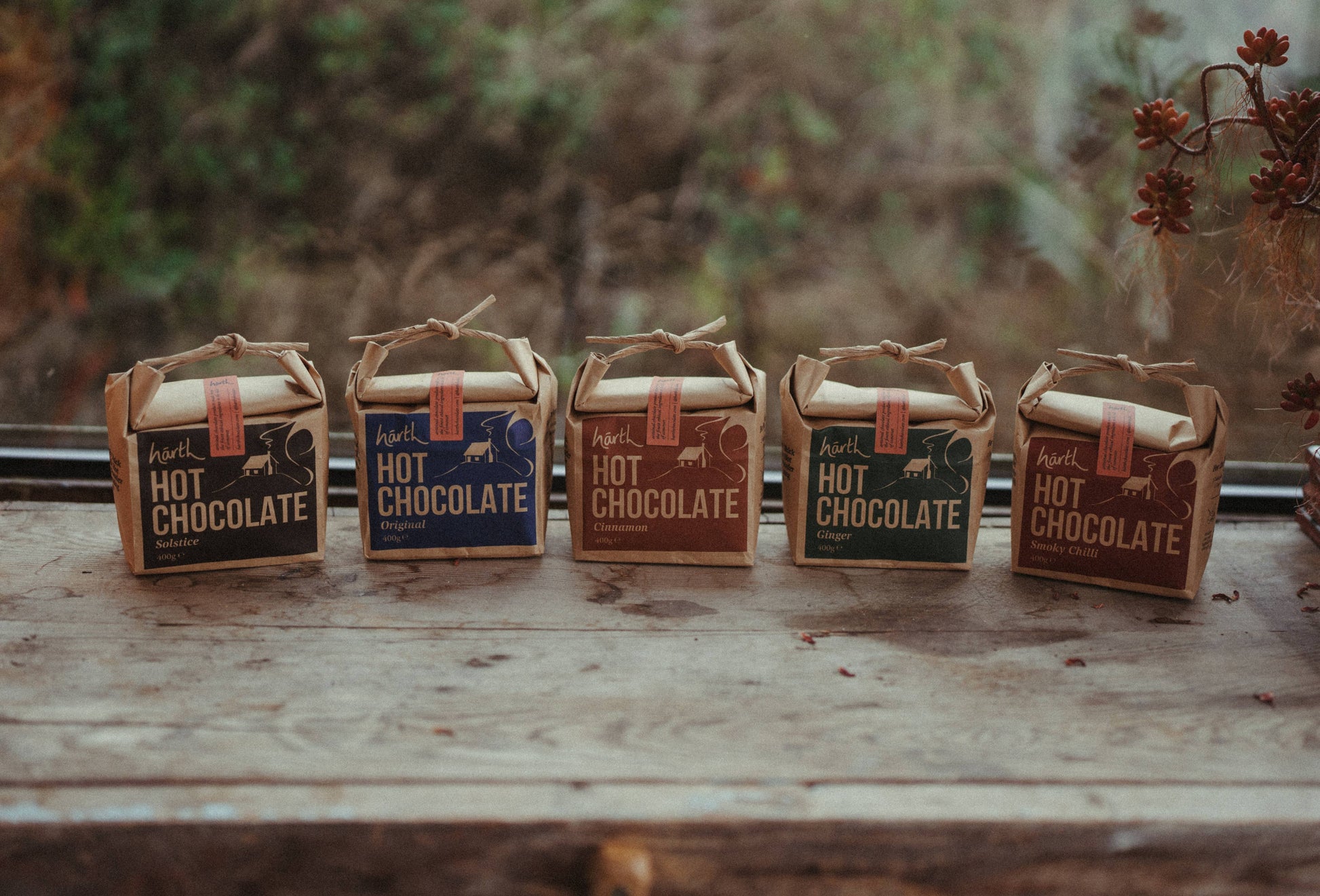 Five small boxes of hot chocolate on a wooden surface with a blurred natural background.