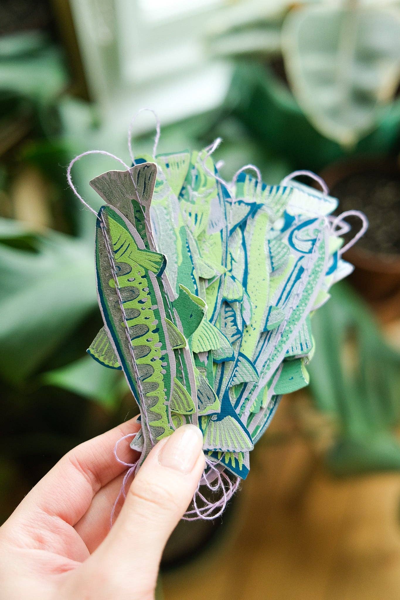 Hand holding a set of colorful paper fish against a blurred green background