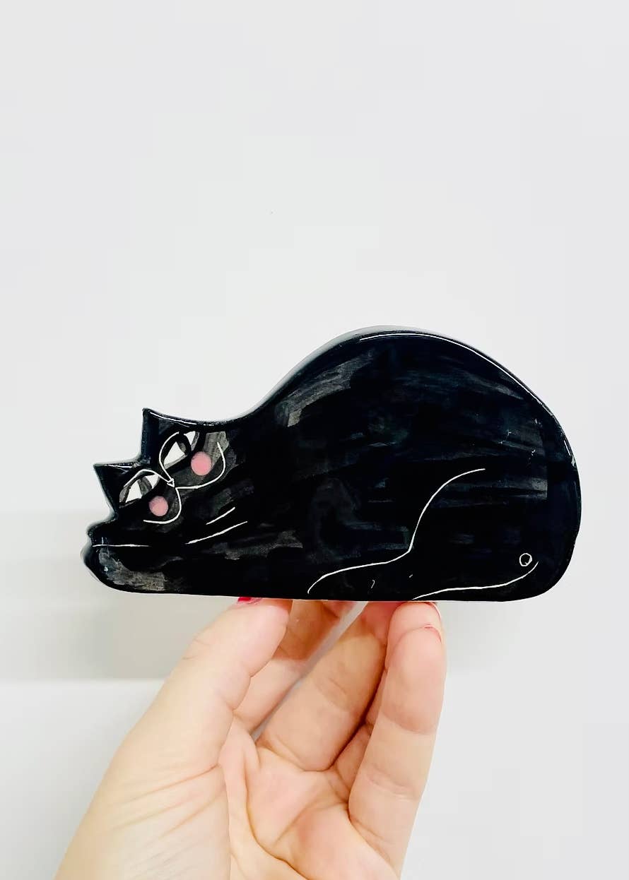 Black cat-shaped object held by a hand against a white background
