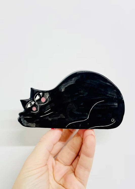Black cat-shaped object held by a hand against a white background