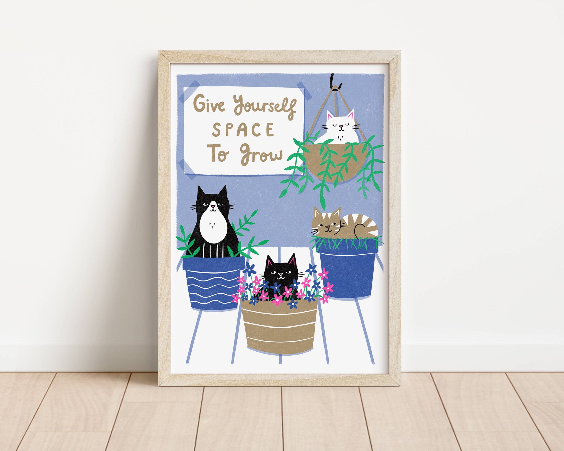 Framed artwork with cartoon cats in plant pots and motivational quote on a white wall.
