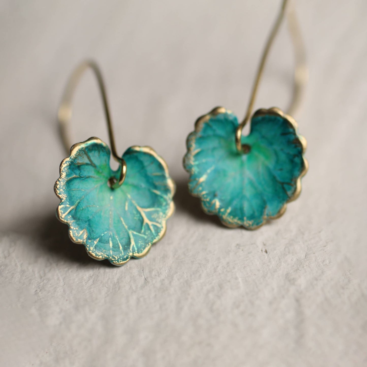 Pair of teal earrings with gold accents on a light gray background