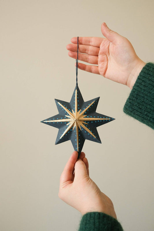 Hand holding a blue star-shaped ornament against a beige background
