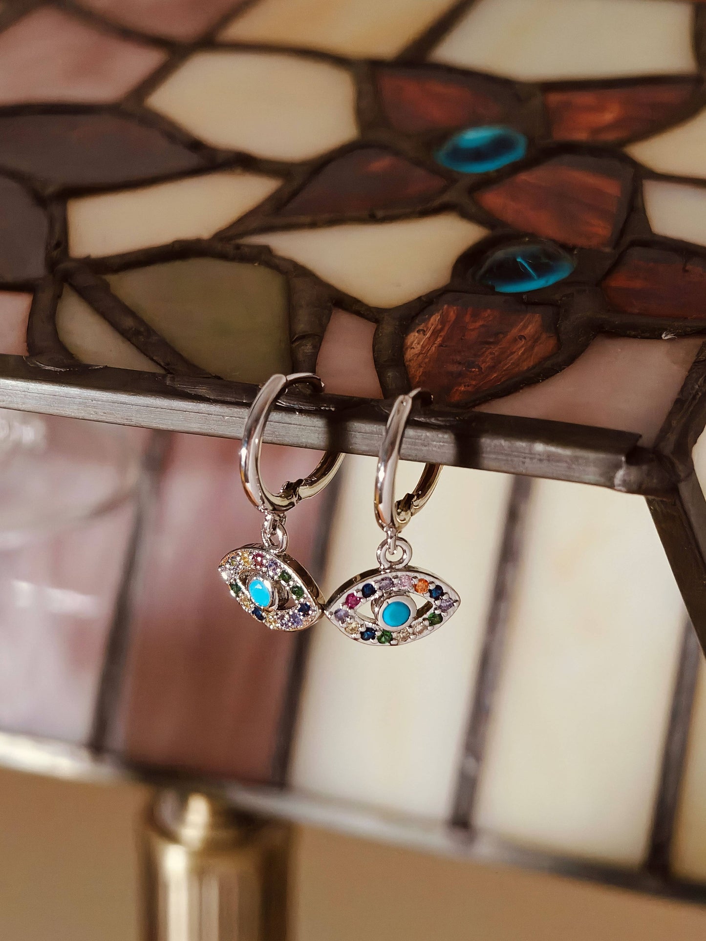 Earrings with eye design in front of a stained glass lamp