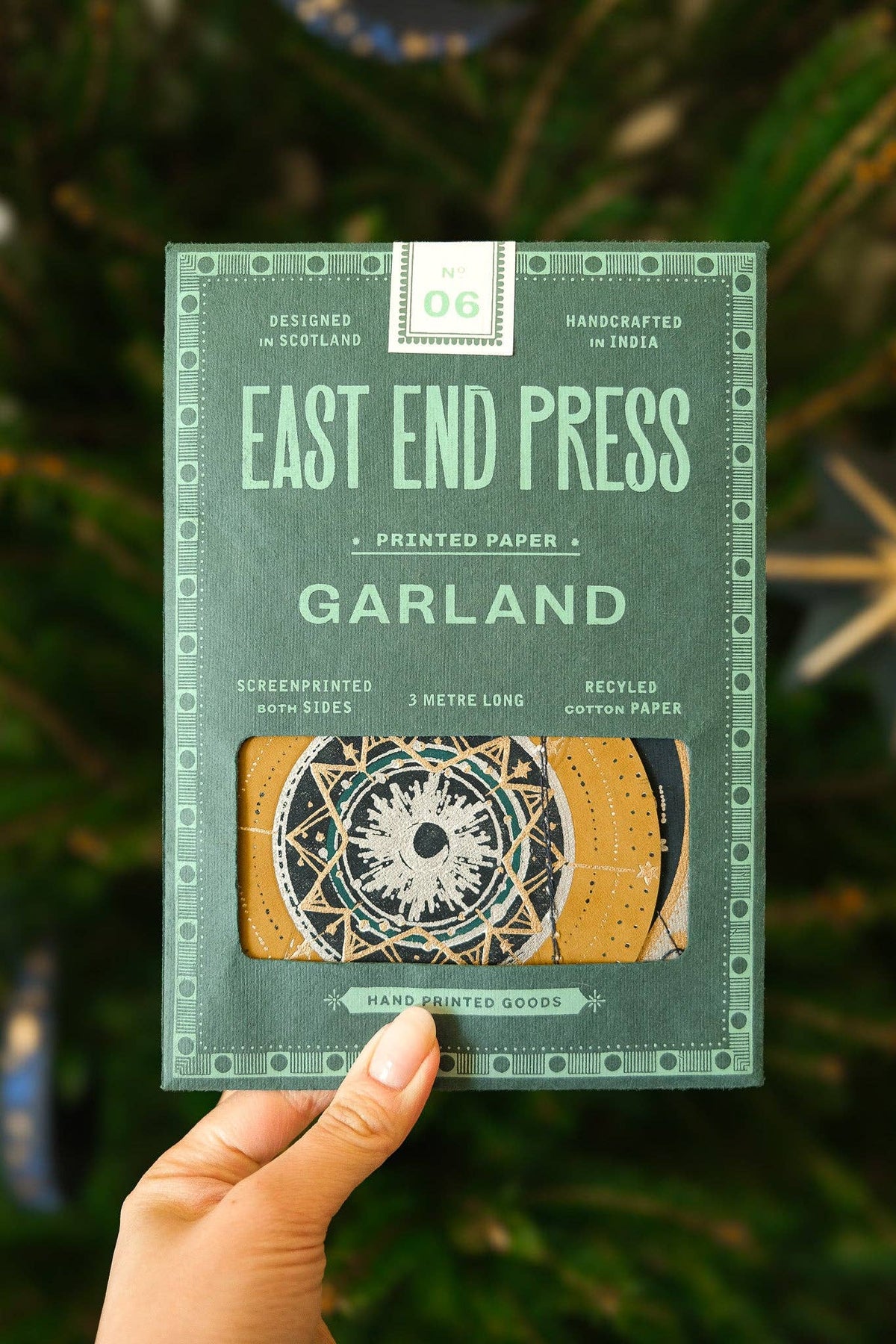 Handheld package of East End Press Garland printed paper with a green background