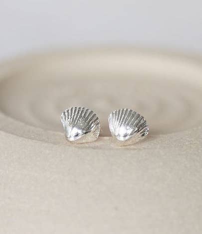 Silver shell-shaped earrings on a beige surface