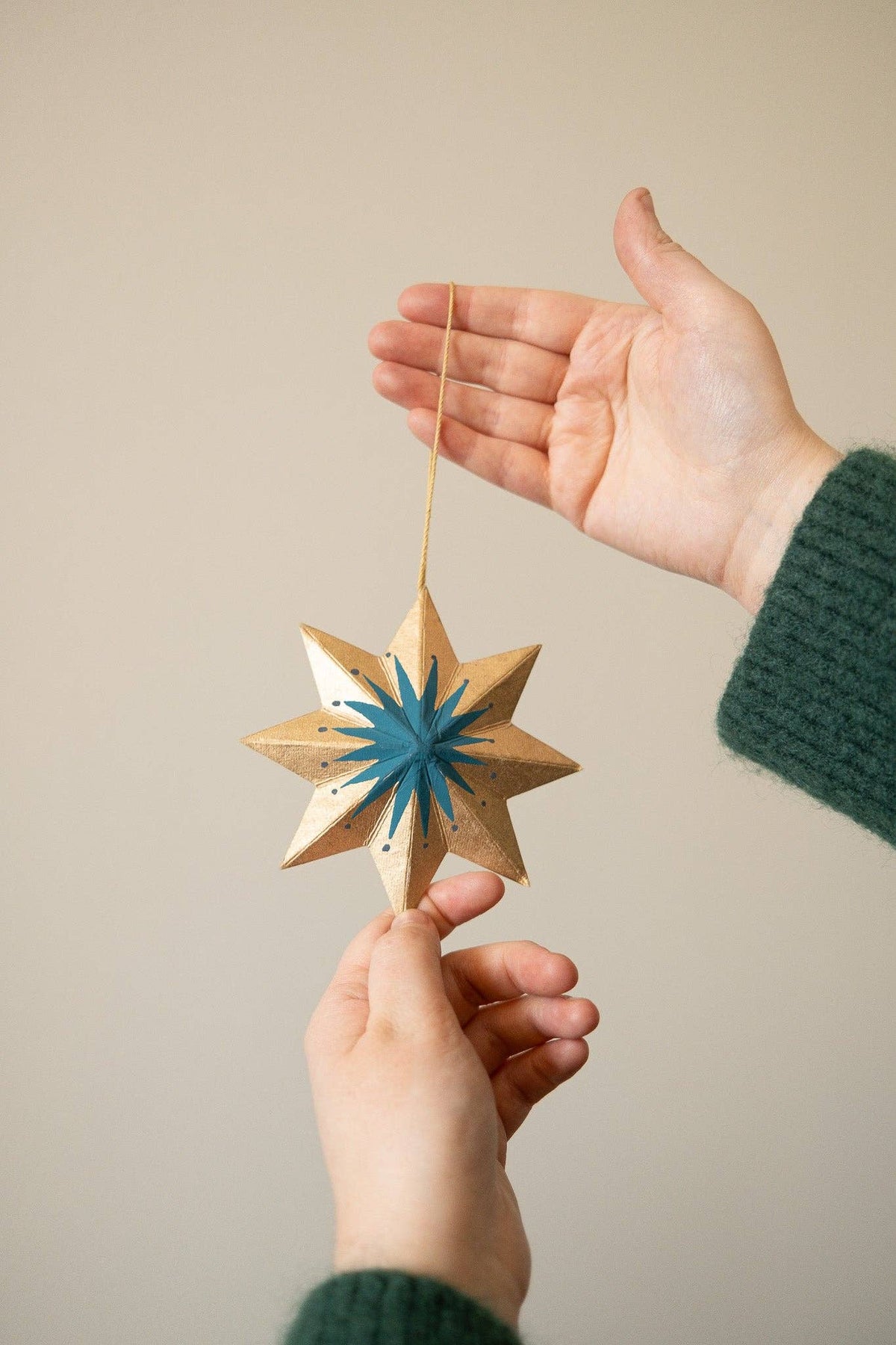 Star-shaped wooden ornament with blue center held by two hands against a beige background