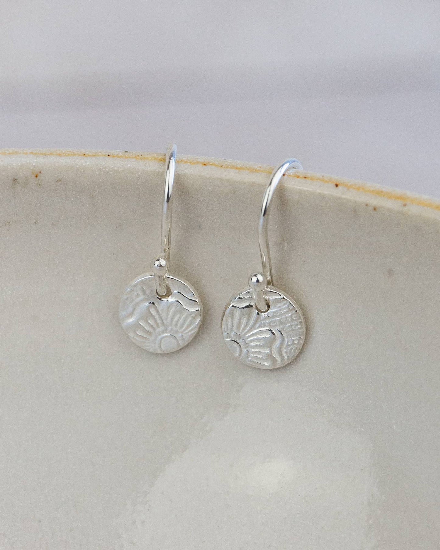 Silver earrings with circular designs on a white dish