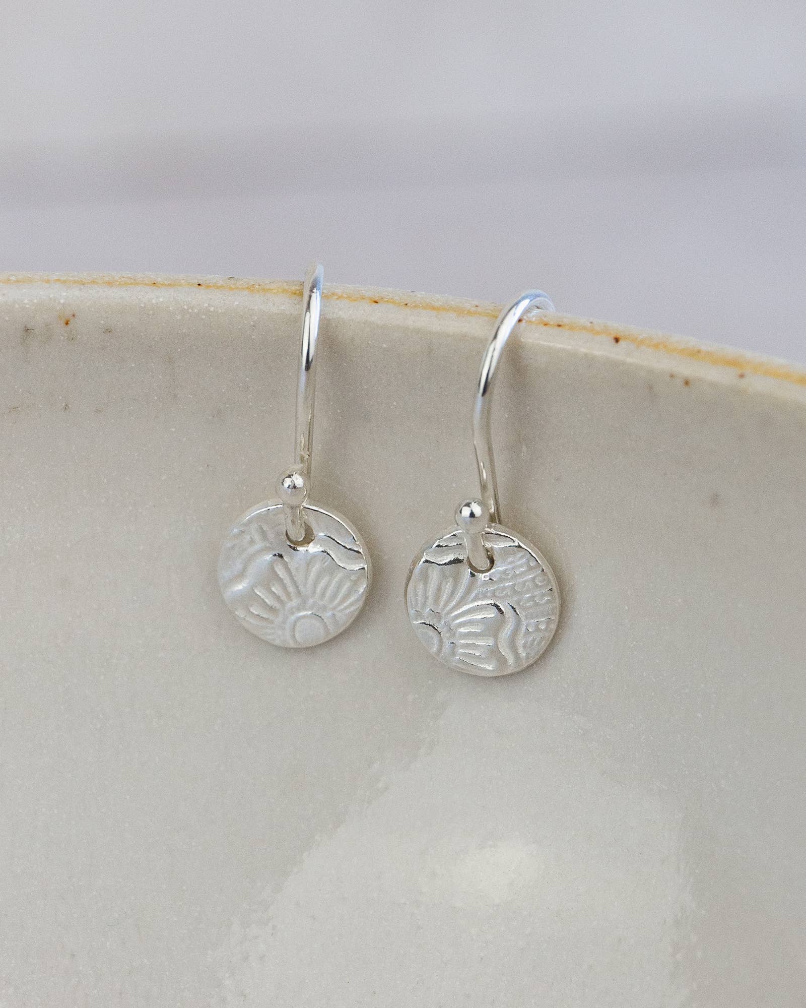 Silver earrings with circular designs on a white dish