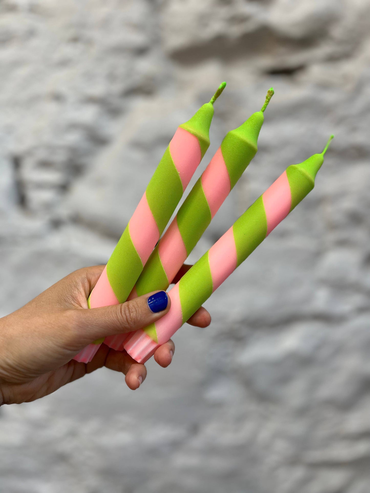 Hand holding pink and green striped candles against a stone background