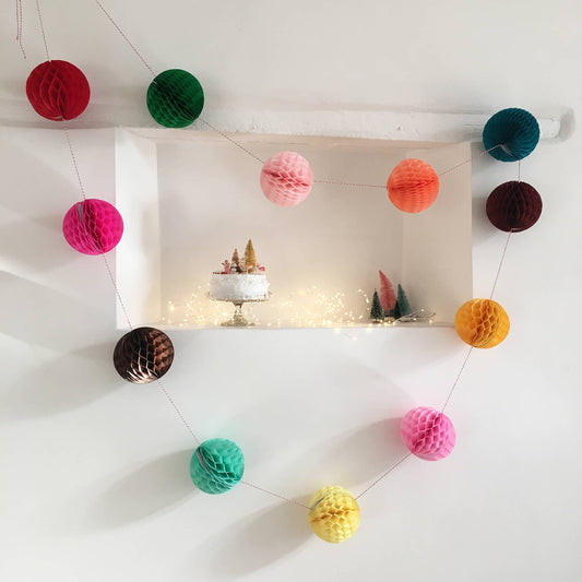 Colorful paper pom-pom garland hanging above a shelf with decorative items.