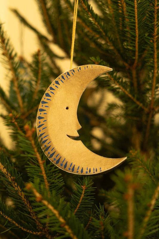 Decorative moon ornament with a face hanging on a Christmas tree.