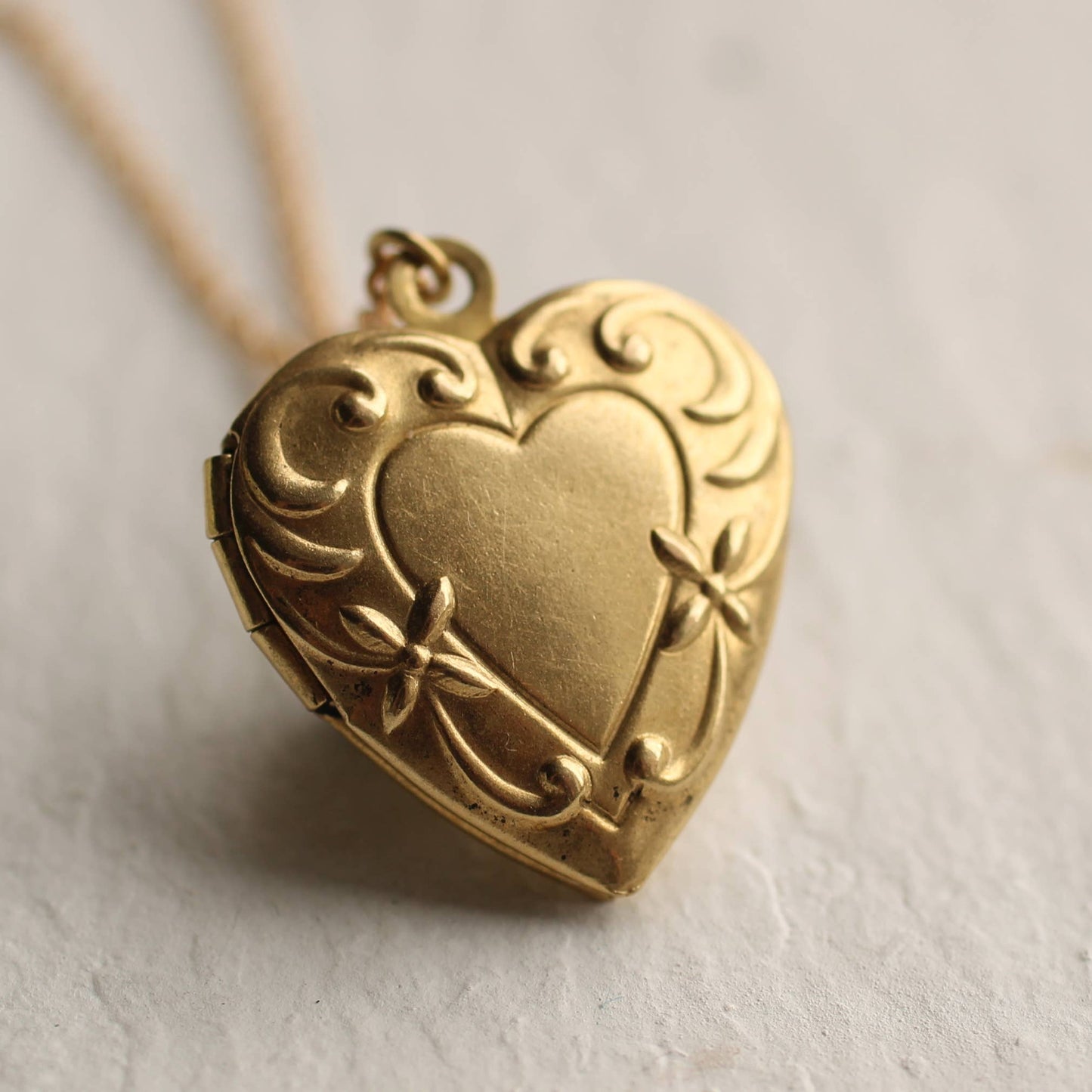 Gold heart-shaped locket with intricate designs on a light background