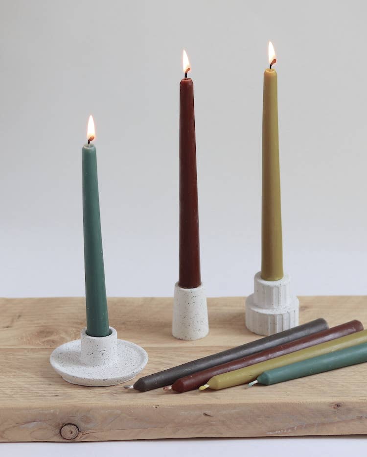 Three concrete candle holders with lit candles on a wooden surface.