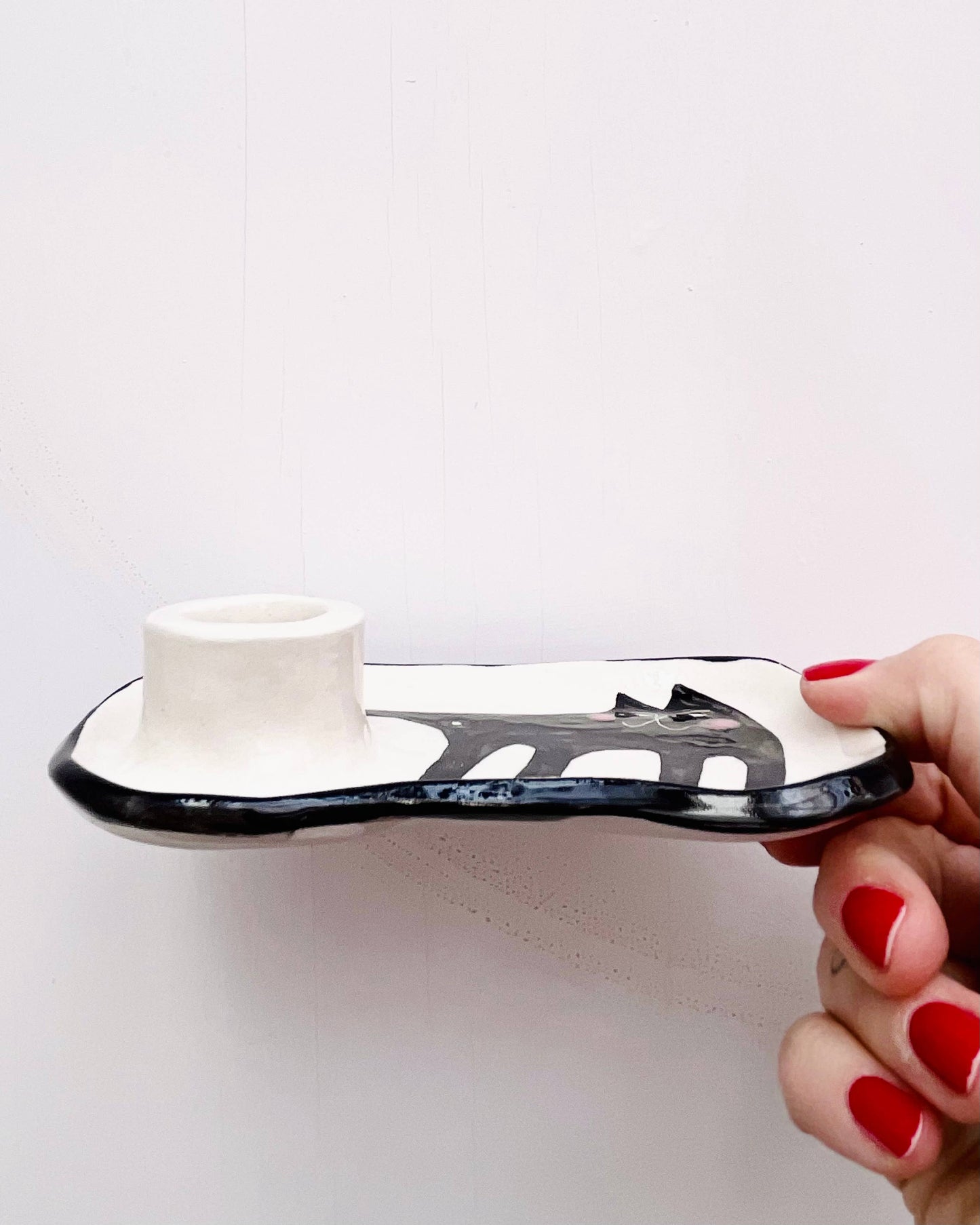 Person holding a white and black ceramic object with red nail polish on a light gray background