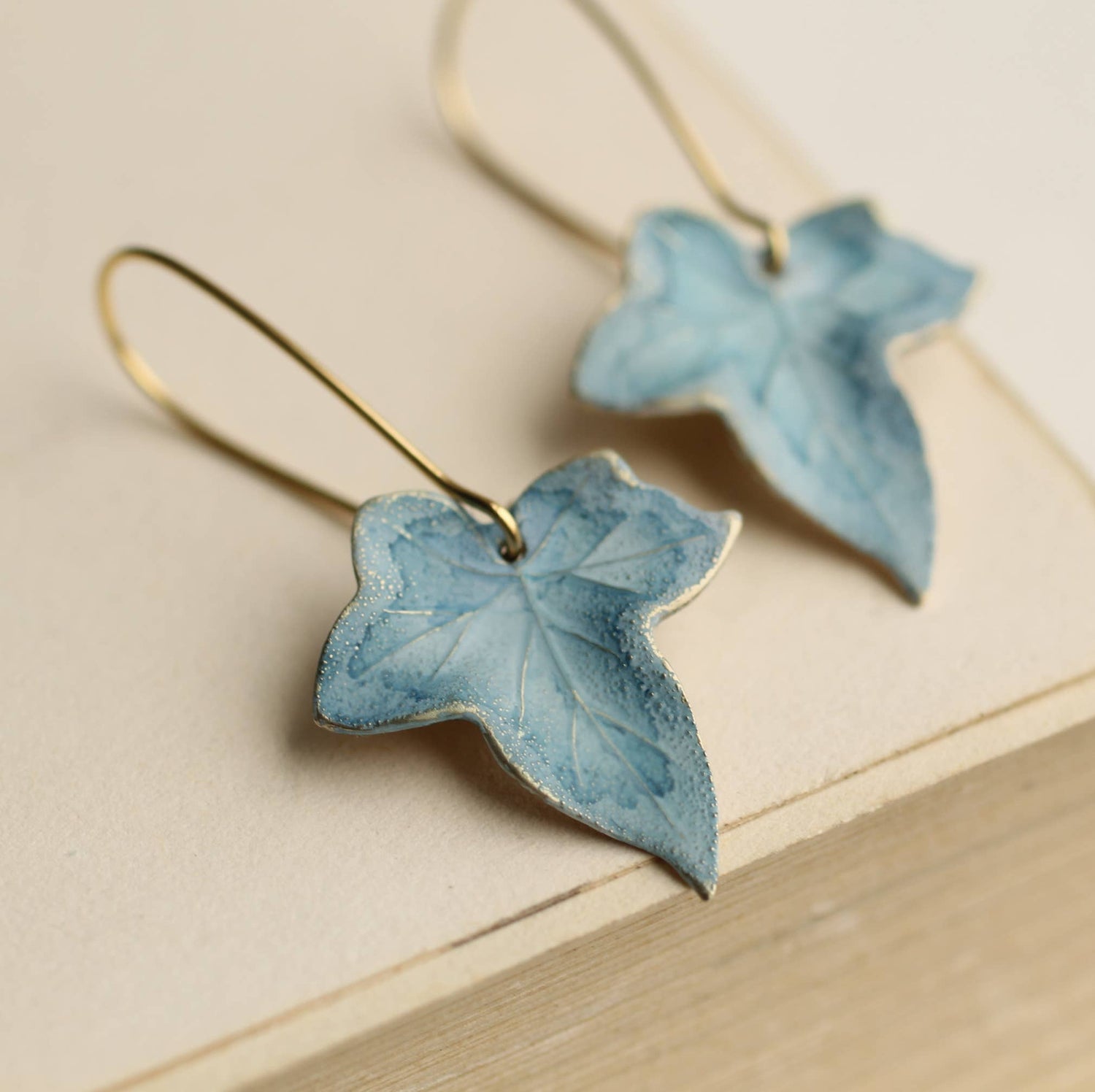 Blue leaf-shaped earrings on a beige surface