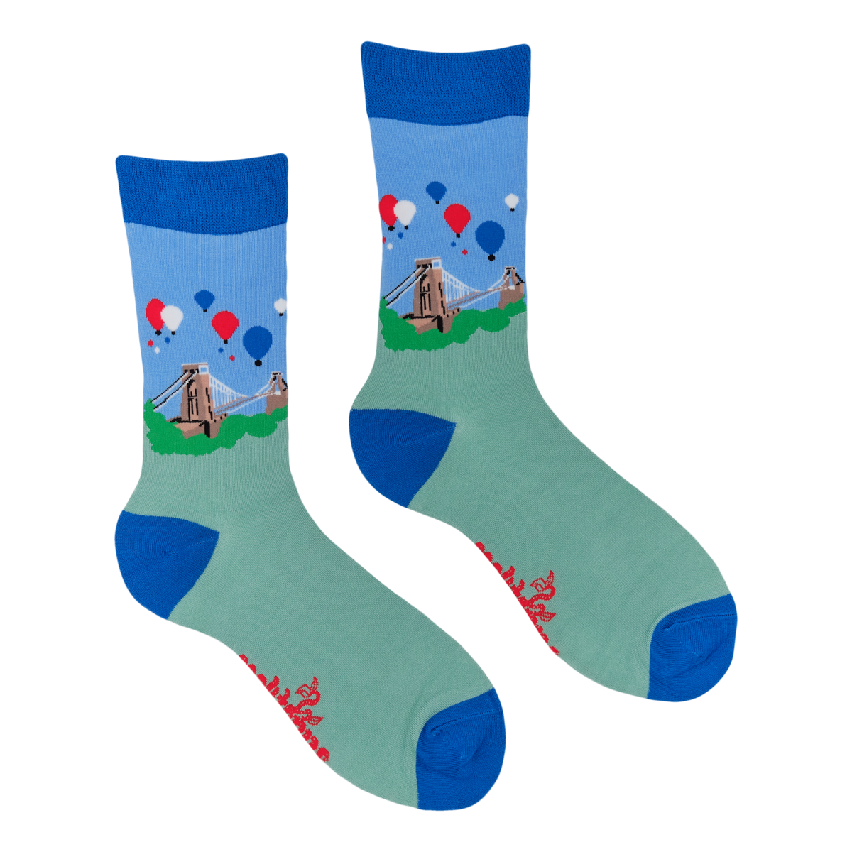 A pair of crew socks with a light blue and mint green base, featuring a printed graphic of a suspension bridge, windmills, and red, white, and blue balloons. The socks have solid blue cuffs, heels, and toes, with red script text near the toes.
