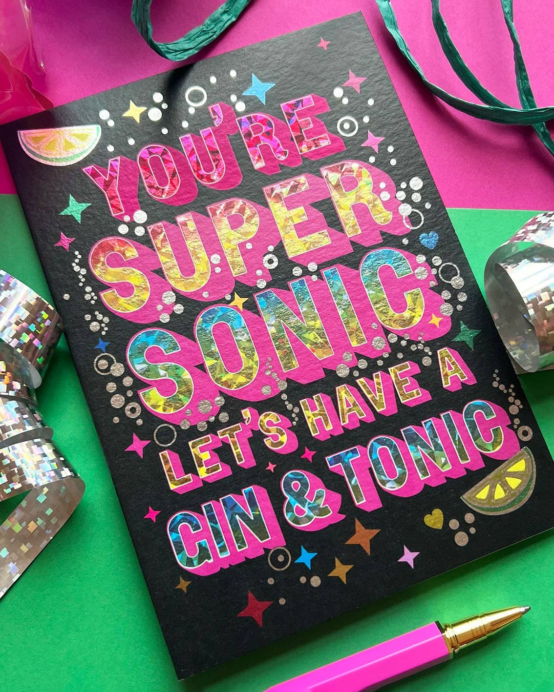 A card with the phrase "You're supersonic let's have a gin & tonic" in a sparkly font surrounded by bubbles, limes and sparkles.