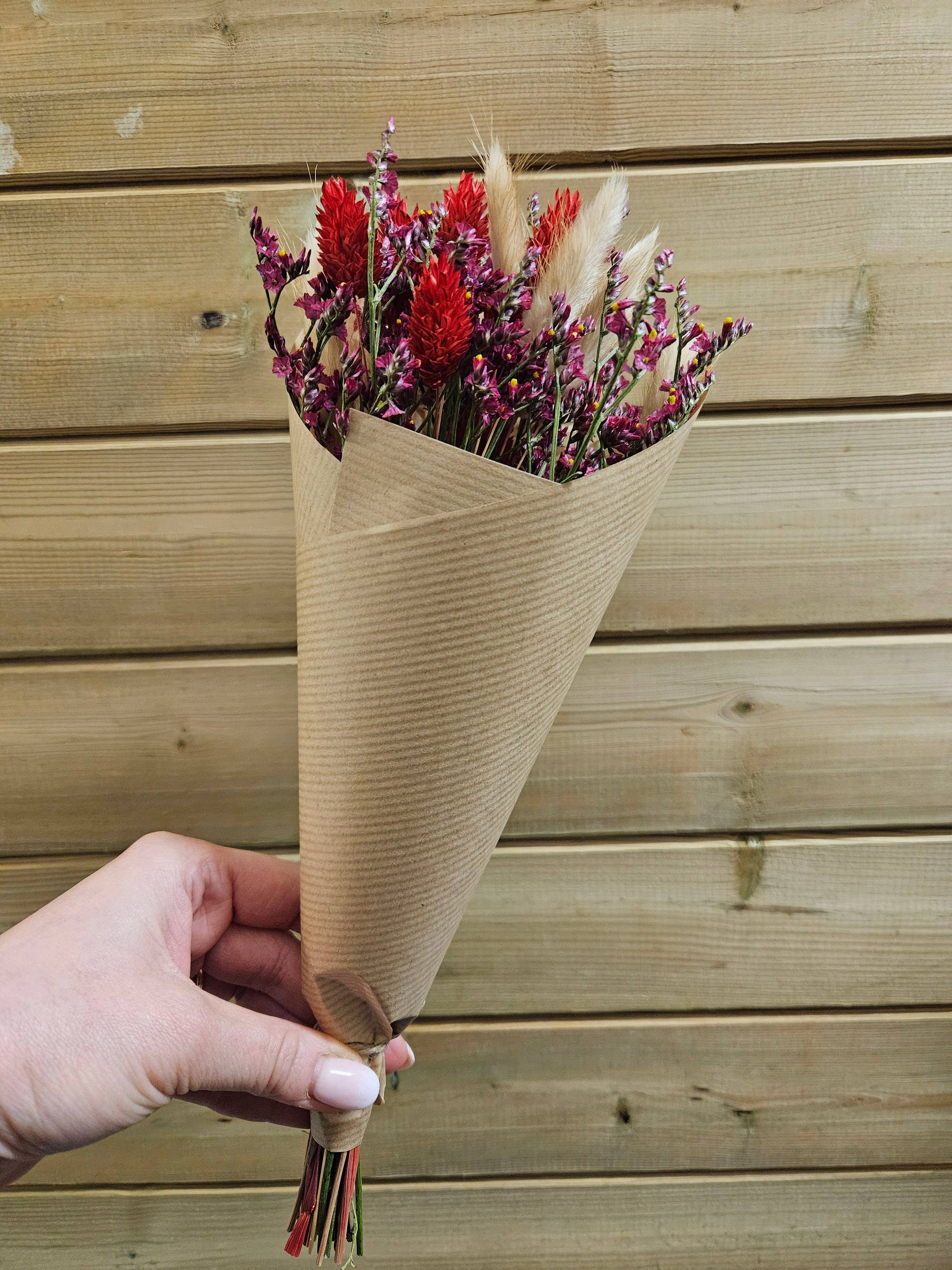 Bouquet of flowers wrapped in brown paper held by a hand against a wooden background