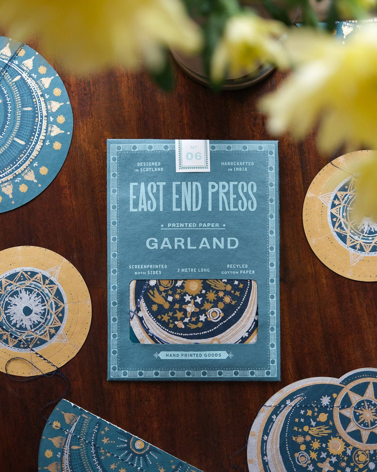Packaging of East End Press Garland product on a wooden surface with decorative items.