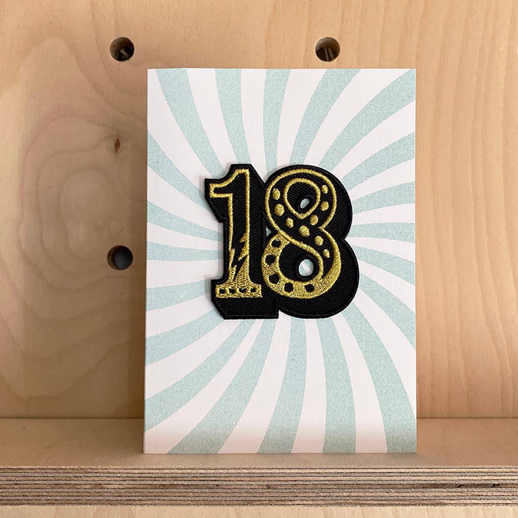 Greeting card with number 18 on a striped background, placed on a wooden surface.
