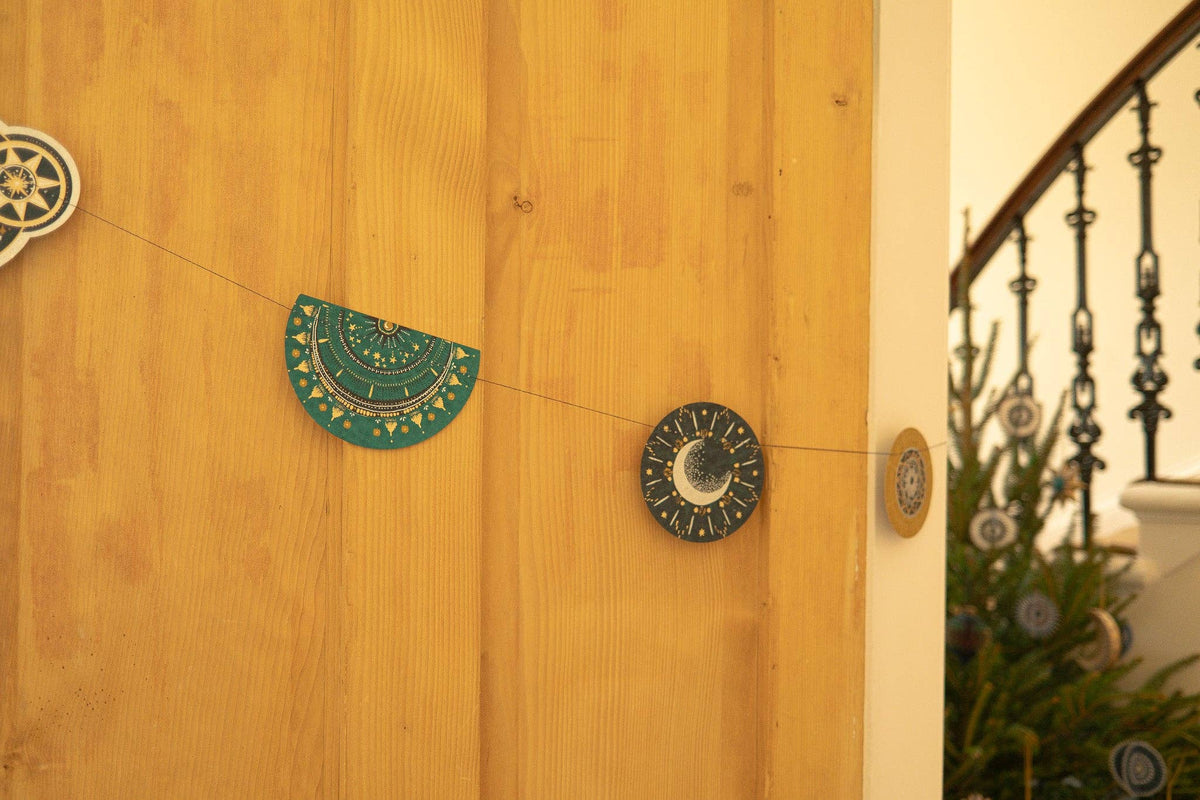 Decorative wall hangings on a wooden wall with a staircase and Christmas tree in the background.