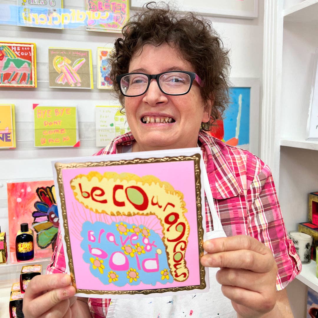 Person holding a colorful sign with motivational text in a room with art supplies.