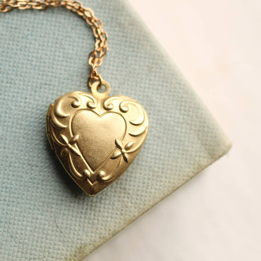 Gold heart-shaped locket on a chain against a light fabric background