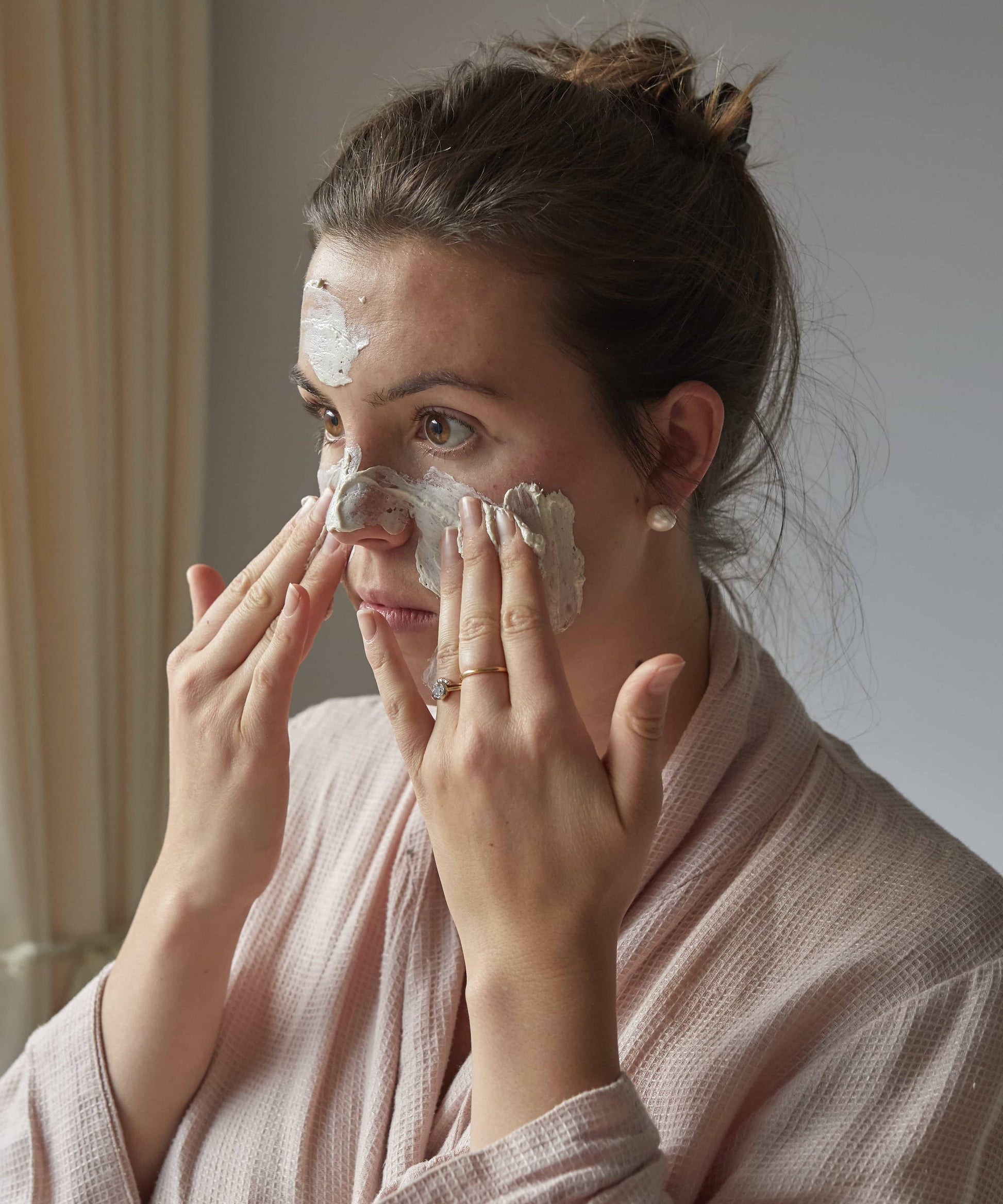 Woman applying cream to her face in a soft, indoor setting