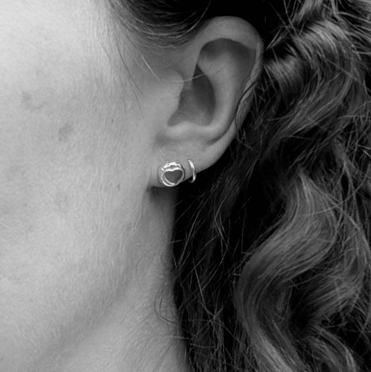 A close-up black and white photo of a person's ear wearing a small silver hoop earring.