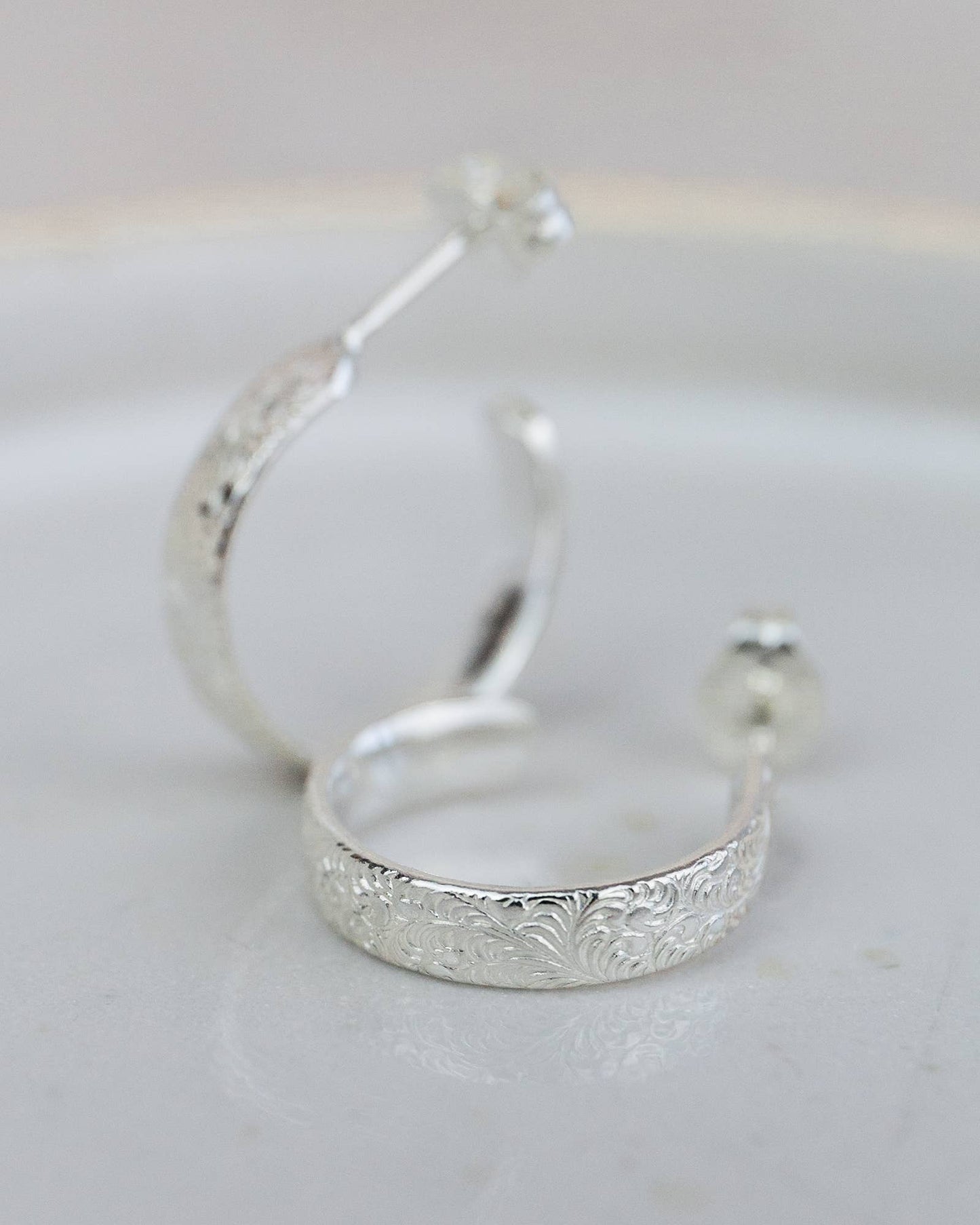 Silver hoop earrings with intricate detailing on a light gray background