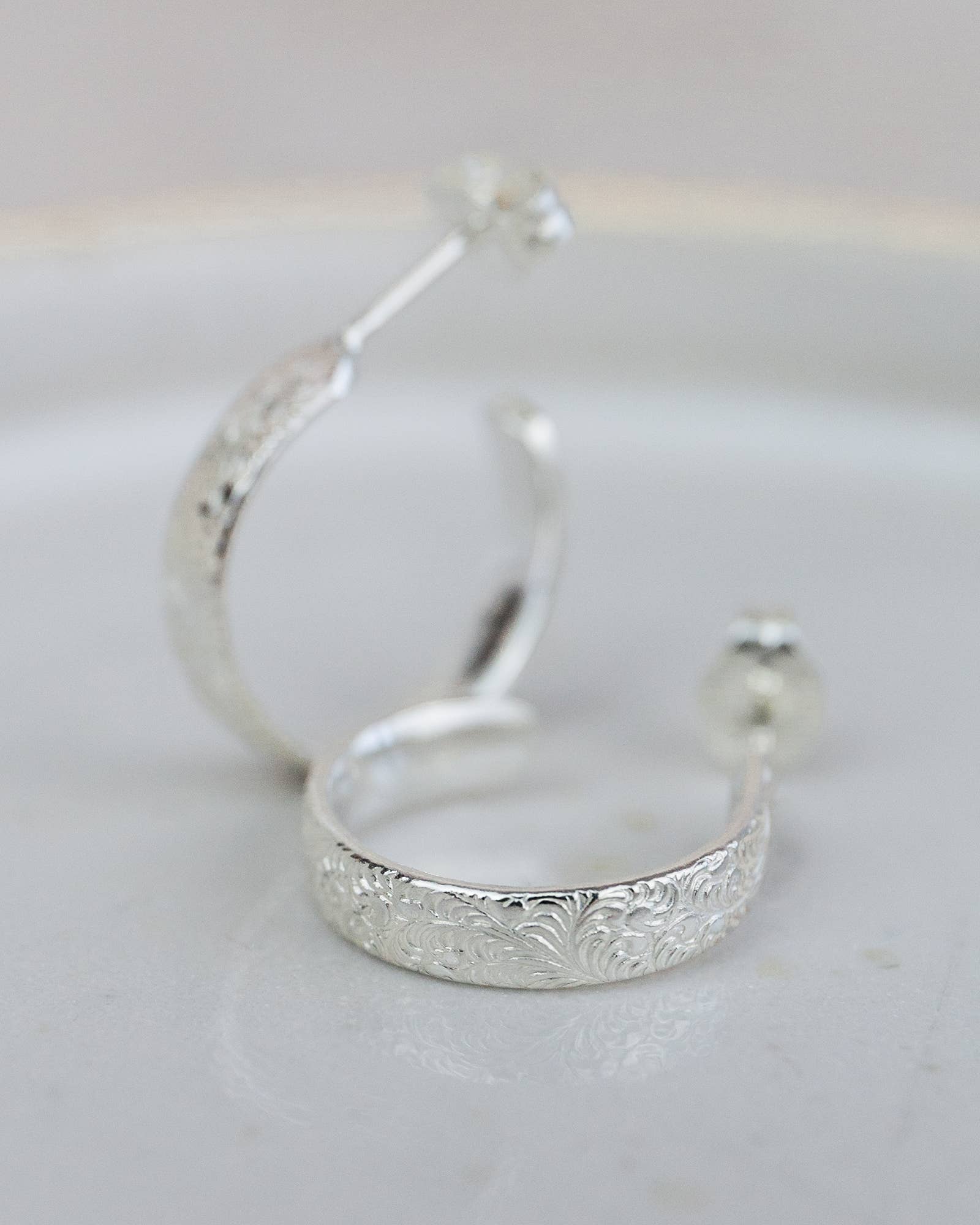 Silver hoop earrings with intricate detailing on a light gray background