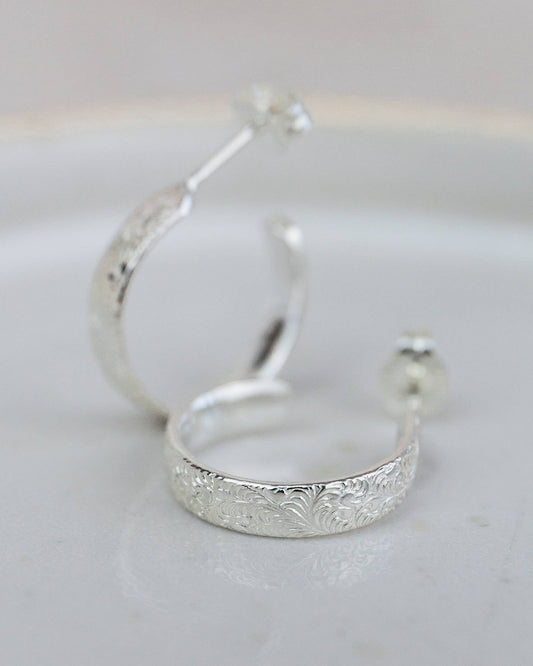 Silver hoop earrings with intricate detailing on a light gray background