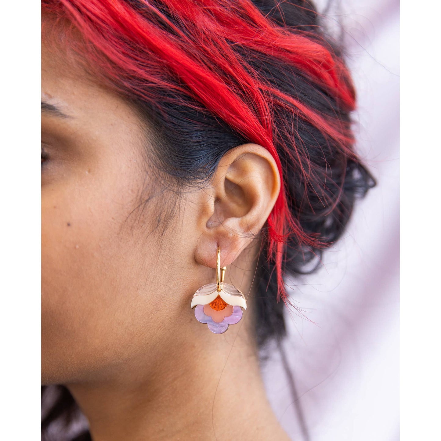Close-up of an ear wearing a floral earring with red, black, and purple hair.