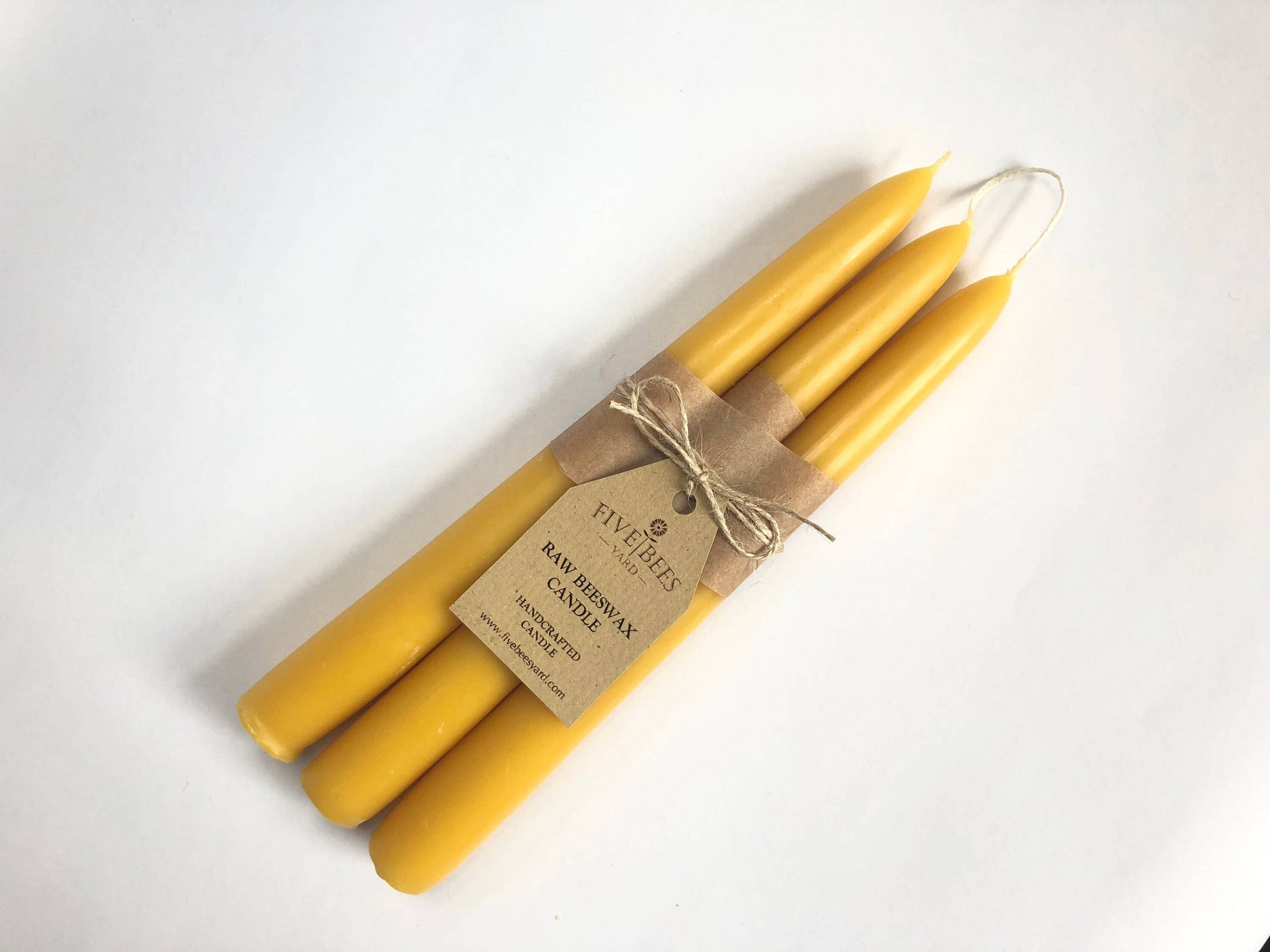 Three yellow candles tied with brown twine and a label on a white background