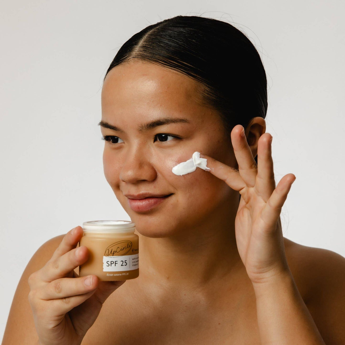 Woman applying sunscreen cream to her face with a jar of sunscreen in her other hand.
