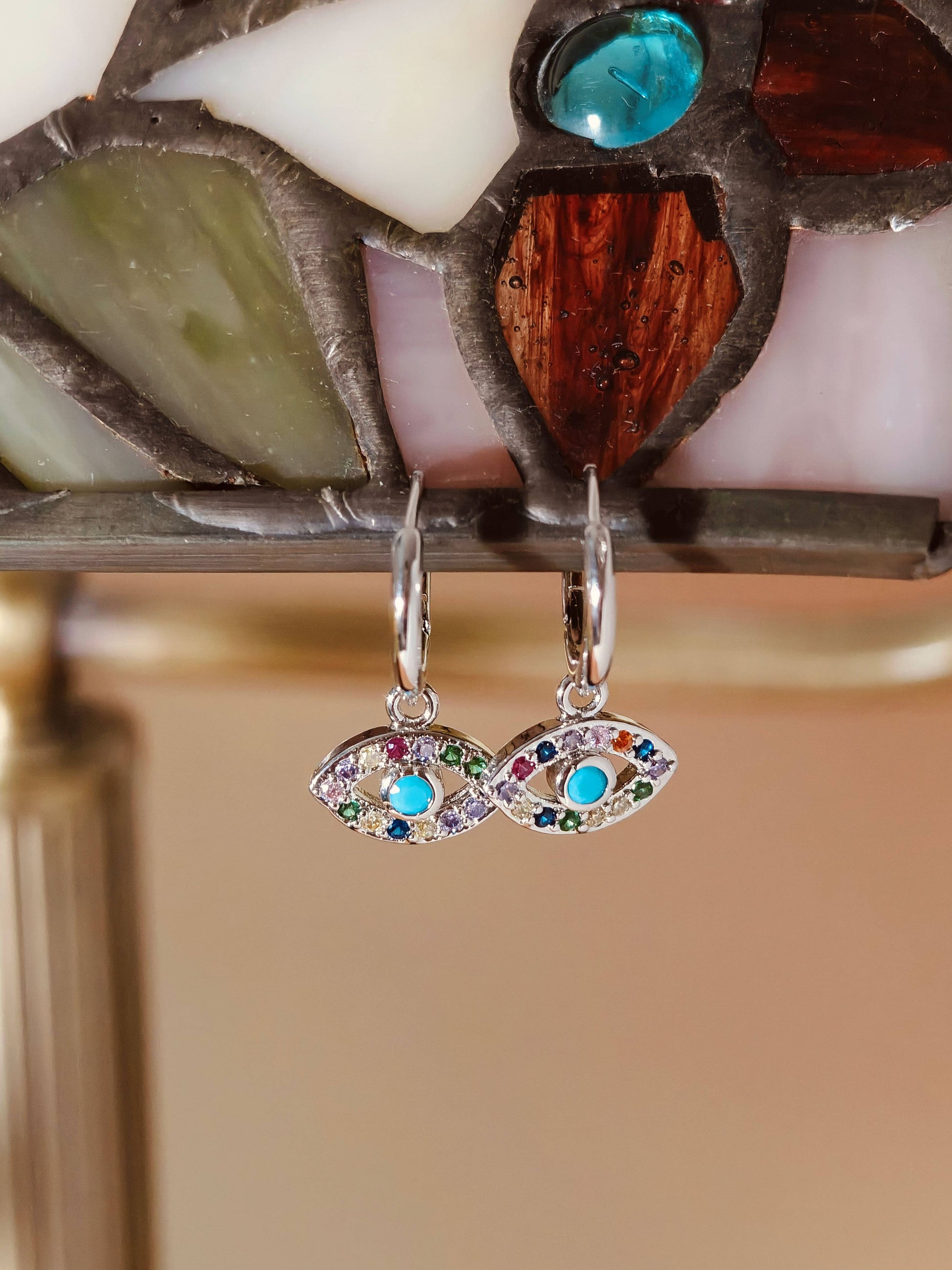 Pair of silver earrings with colorful gemstones hanging in front of a stained glass window.