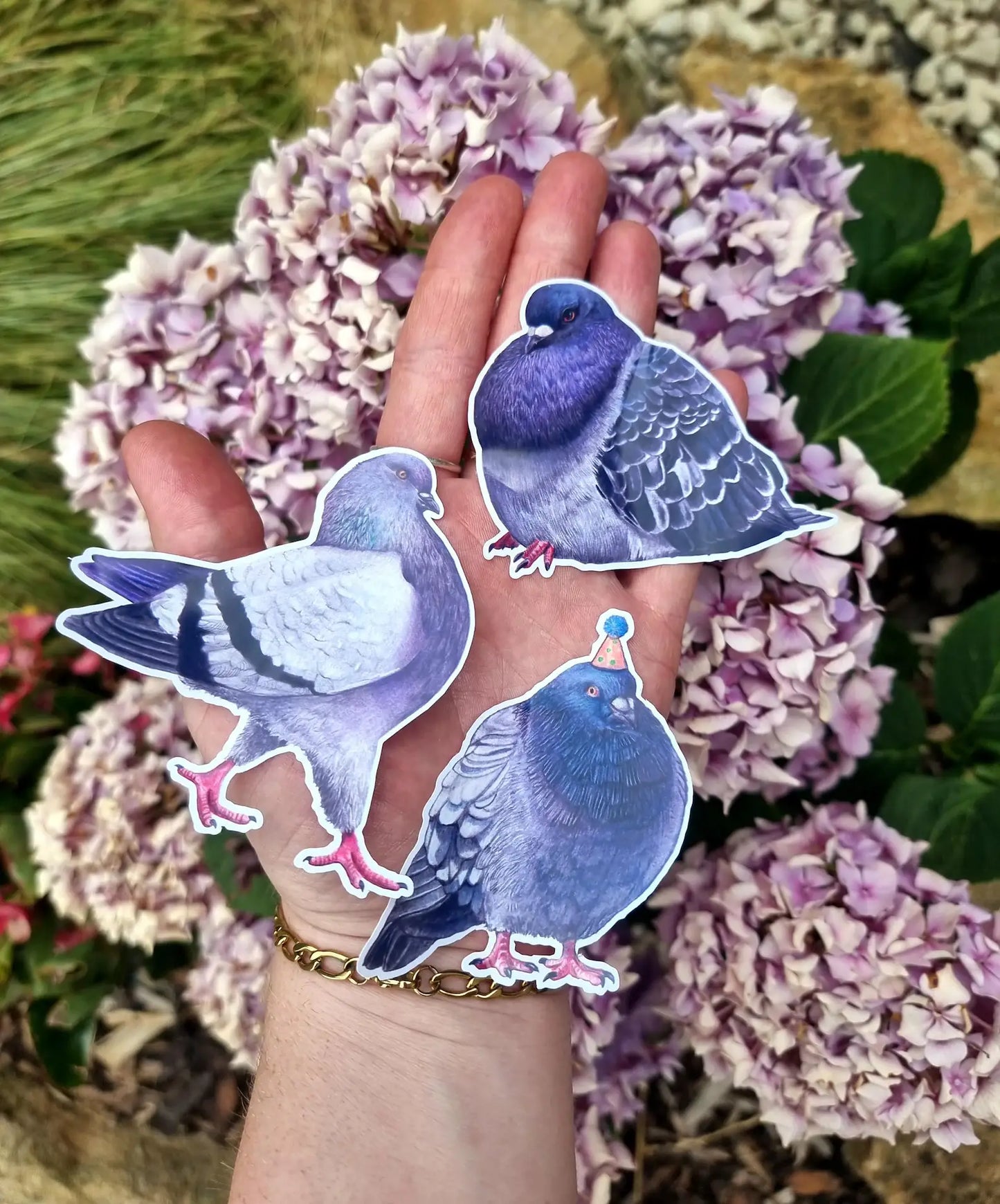 Hand holding three pigeon stickers with a background of pink flowers