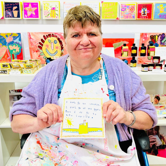 Person holding a piece of art in an art studio with colorful cards and supplies on the wall.